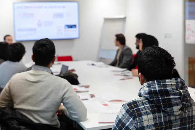 students sitting around a table at business clinic watching presentation on screen