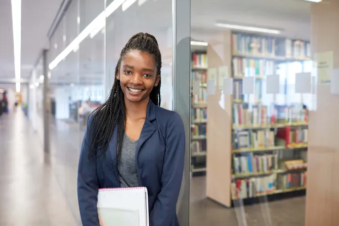 A student standing in the library, holding a book.