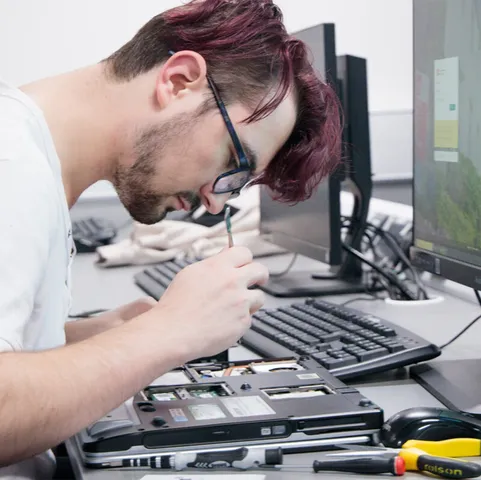A student works with tools including different types of screwdrivers on the electronics of a laptop