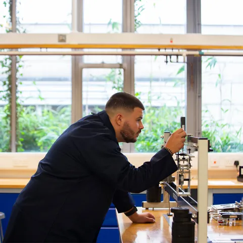 A student in navy overalls focuses on a piece of table-top mechanical equipment in an engineering workshop