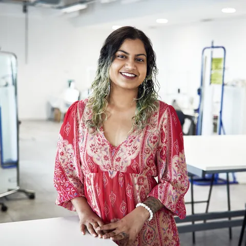 A fashion student wearing a pink dress and with black and blonde did-dyed hair smiles at the camera from a fashion workshop at USW Cardiff