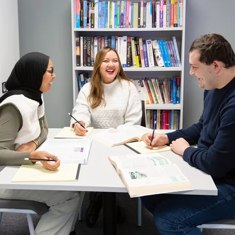 Three psychology students sitting at a table happily working on a university project