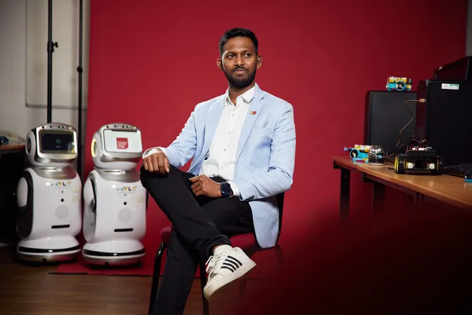 Student Noel Anthony sitting in front of red backdrop with robots behind