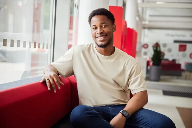 Social Policy PhD student Abasiokpon smiles for camera while sat on the red sofas of the business school foyer