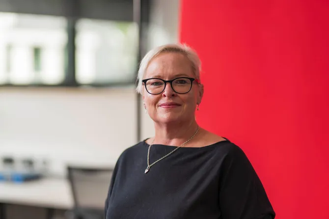 Deborah Lancastle smiling at the camera against a red backdrop.