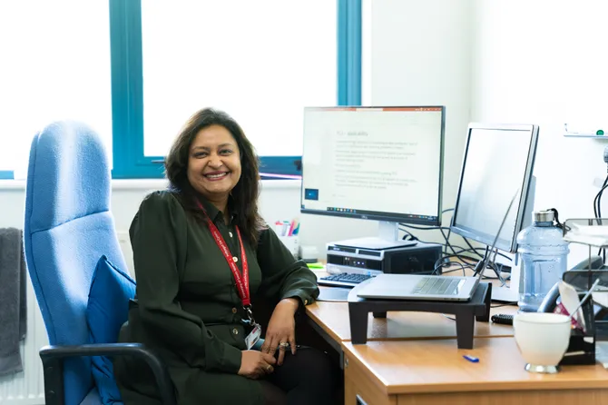 member of University staff sitting at a computer, smiling to camera
