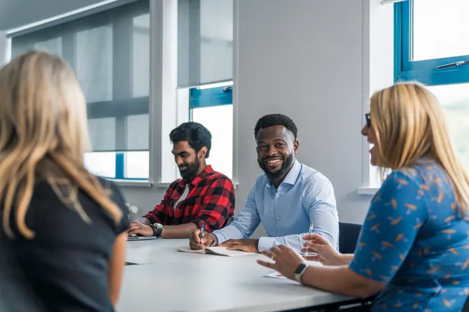 four members of university staff working and having a conversation, smiling