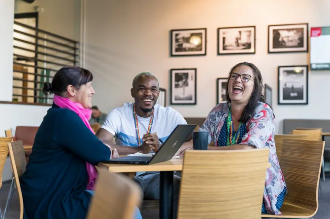 three members of the equality, diversion and inclusion team sitting at a table having an informal meeting, laughing and smiling