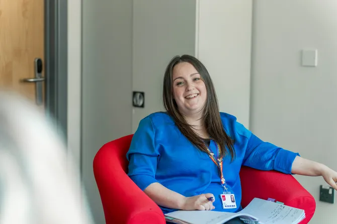 a member of the faculty of business and creative industries team sitting in a red chair smiling