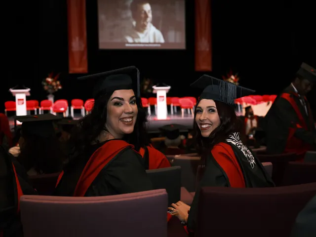 Two graduates wearing full academic dress and graduation caps in a graduation ceremony.