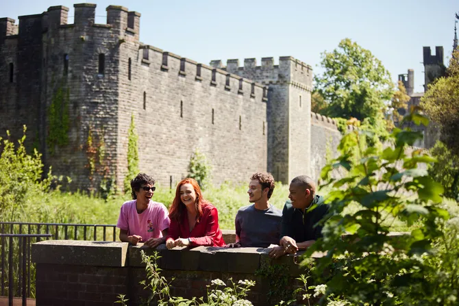 A group of students sitting in Bute Park with Cardiff castle in the background.