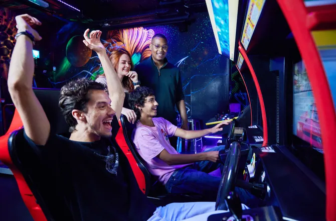 A group of students celebrating over winning a racing car game at an arcade bar.