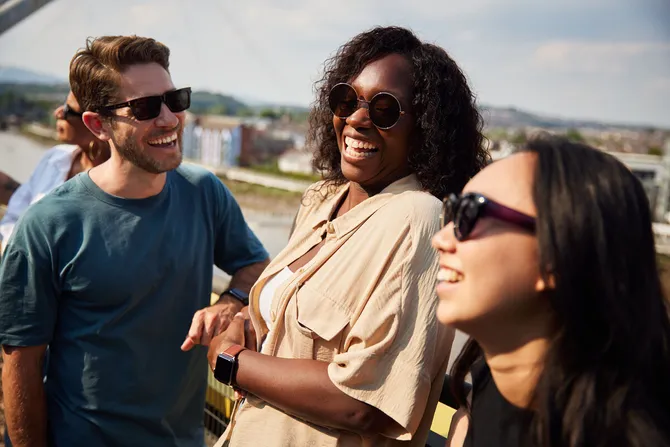 Three smiling students wearing sunglasses on Newport Riverfront.