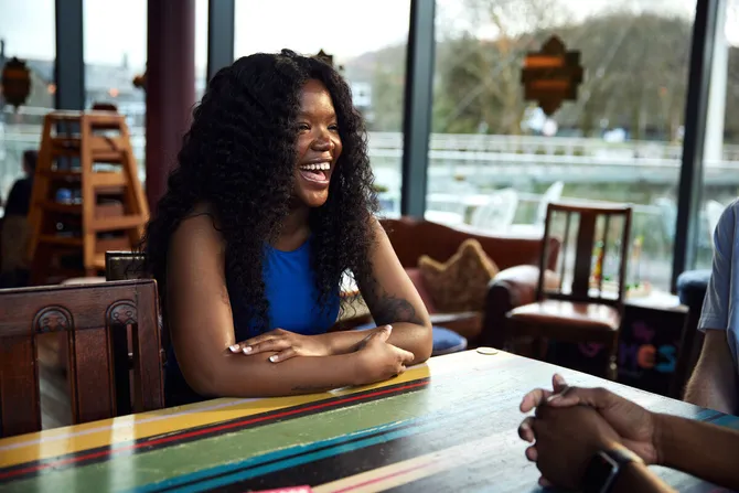 A student smiling while chatting with their friends at a restaurant in Pontypridd.