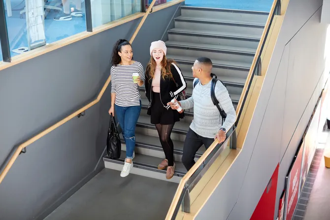 Three students walking together down a staircase, talking and holding their drinks.