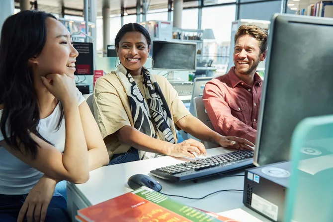 Three students sat together working at a desktop computer.