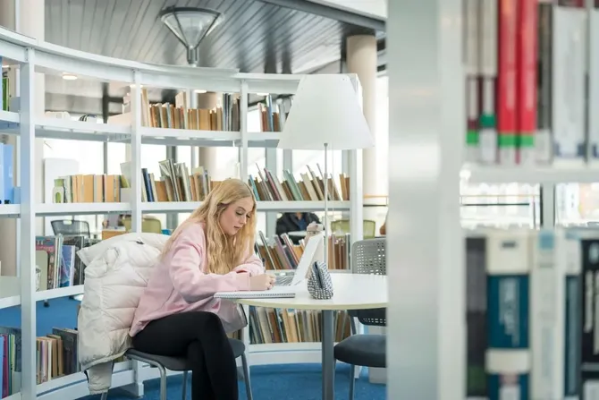 student sitting at a desk amongst the books at newport campus library