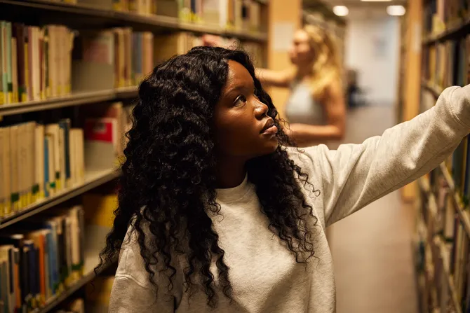 A close up of a student selecting a book from the bookshelf in the library.