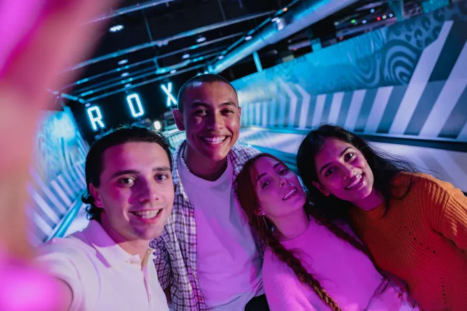A group of four students are taking a selfie at a bowling alley named Roxy Lanes in Cardiff. There are neon lights lighting the room.