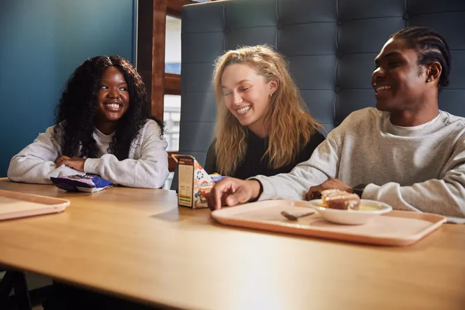 Three students laughing, sat down at a table in Stilts