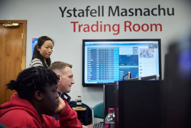 Lecturer surveying students in the Trading Room, accounting data is displayed on the classroom board.