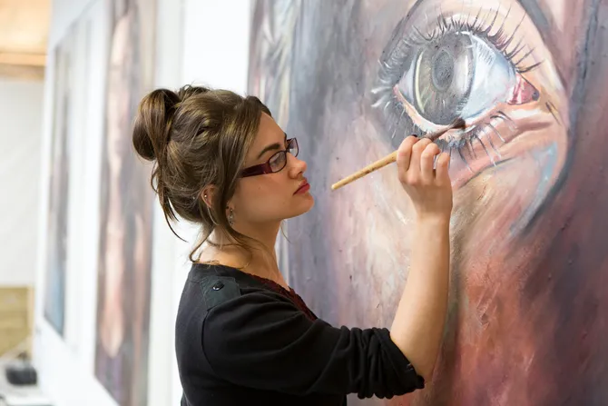 female student painting a large scale painting of a face in vivid colours