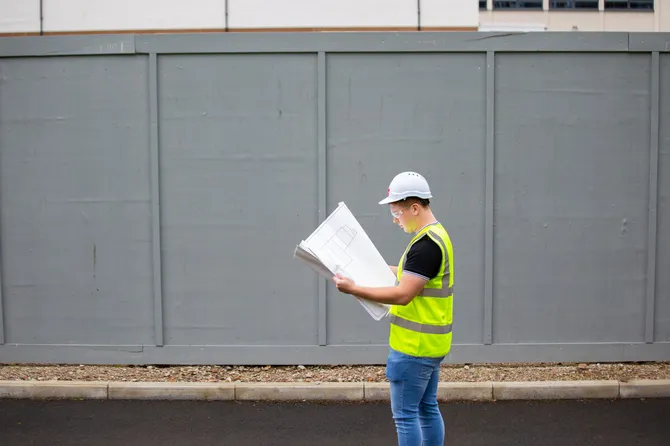 A person in a hi-vis and a hard hat is stood reviewing documentation.