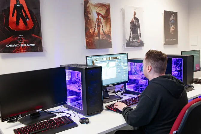 computing student working at computer, with images of video games on the wall above