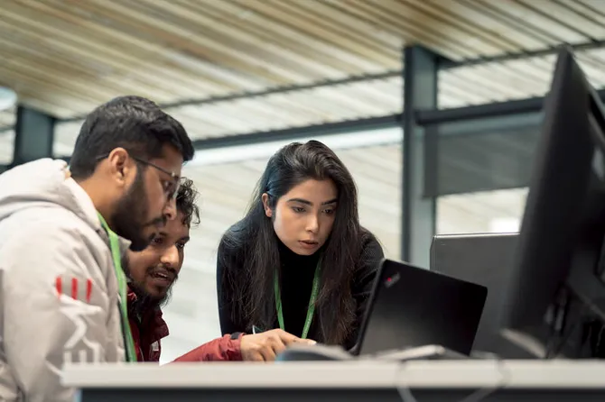 Three students looking at a laptop together and pointing at the screen.