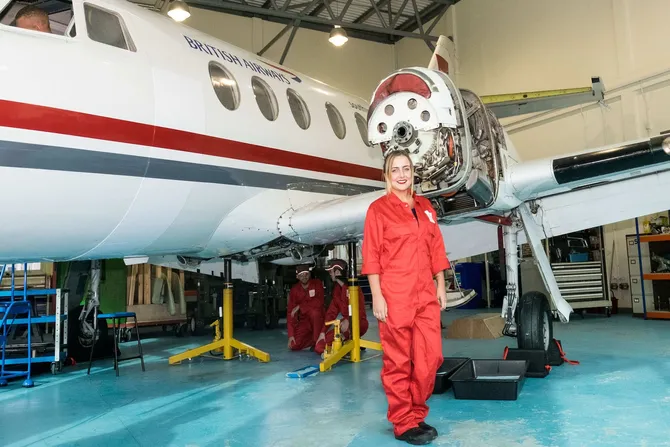 Aerospace Engineering graduate Katie Danahar stands in front of the small aircraft at the Aerospace Centre in Treforest while wearing a red engineering jumpsuit