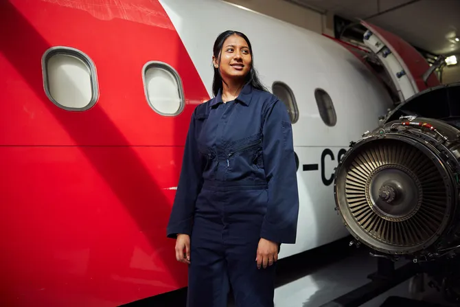 Student, Pooja Umashankar, stood in front of an aeroplane wearing engineering workshop uniform.