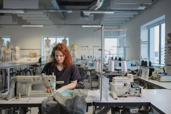 Fashion student sitting at a desk using a sewing machine.