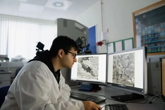 Forensic student wearing a lab coat, studying evidence on a computer screen