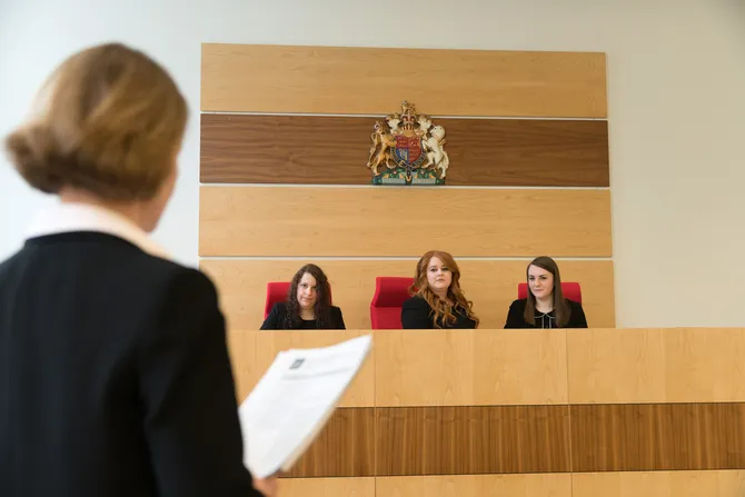 three students have taken seats in the moot court stand, they are listening to a statement being presented.
