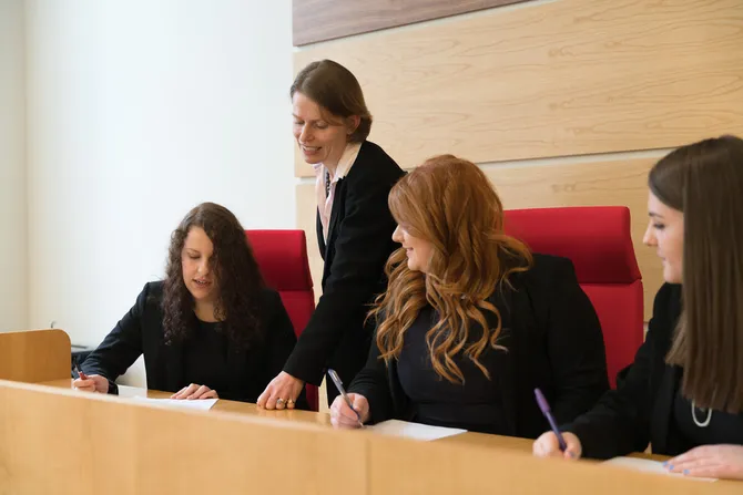 An academic is supervising three students who are sat with papers in the moot court booth.