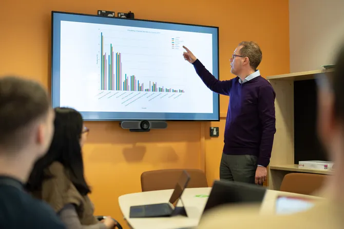 An academic is presenting bar charts to students in a classroom.