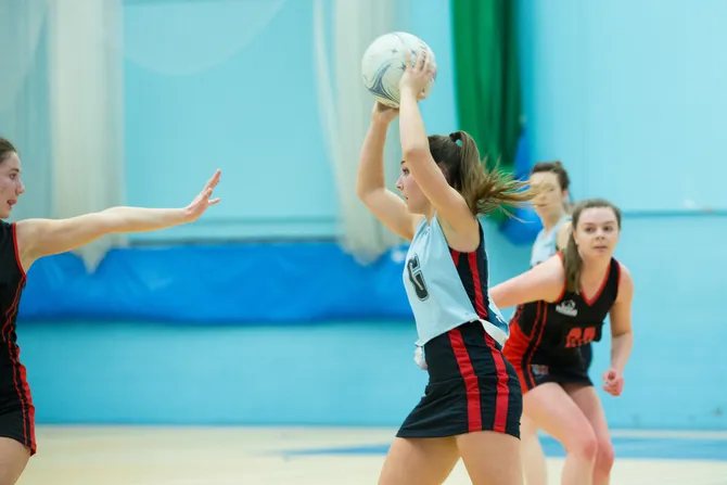 A student is holding a netball above their head about to make a pass.