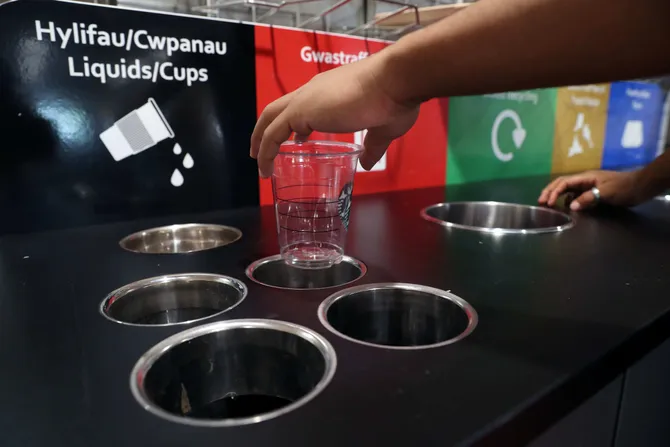 A close up of a hand placing a plastic cup into a recycling bin
