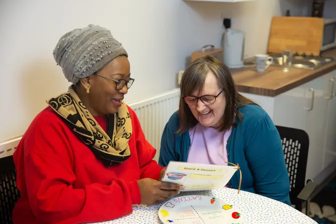 A student studying learning disability nursing reads a menu to a patient in a cafe