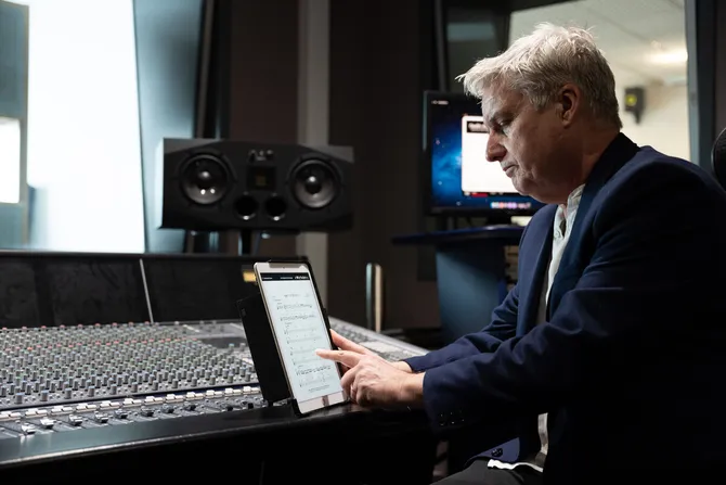Professor Paul Carr reads sheet music on a tablet in front of a mixing desk in a recording studio