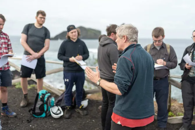 A group of students listening to an academic talk on a geology field trip.