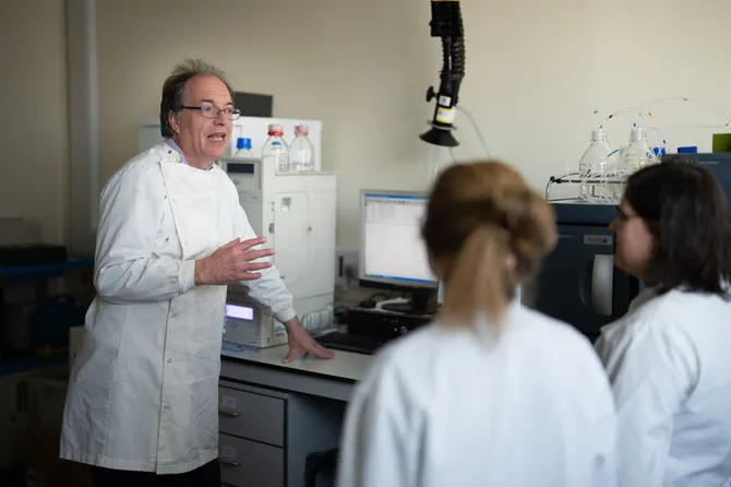 Researchers in white lab coats discussing data on a computer in a research lab.