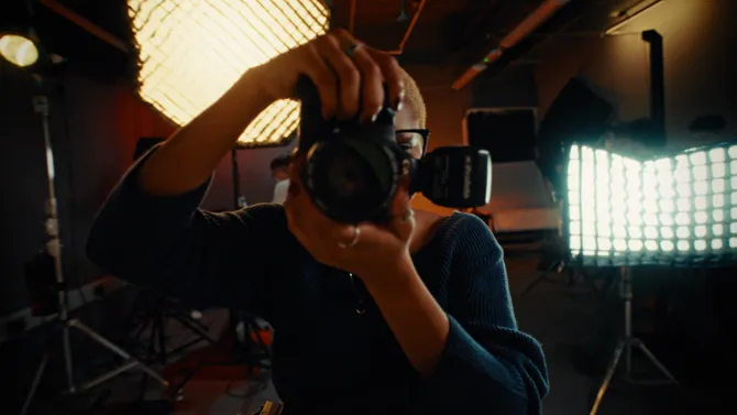 A student taking a photo with a camera, standing in front of a light box in a studio.