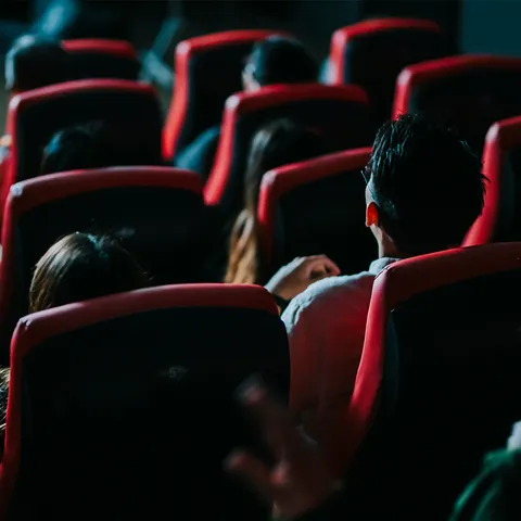 Two people sat in a dark cinema screen watching a movie