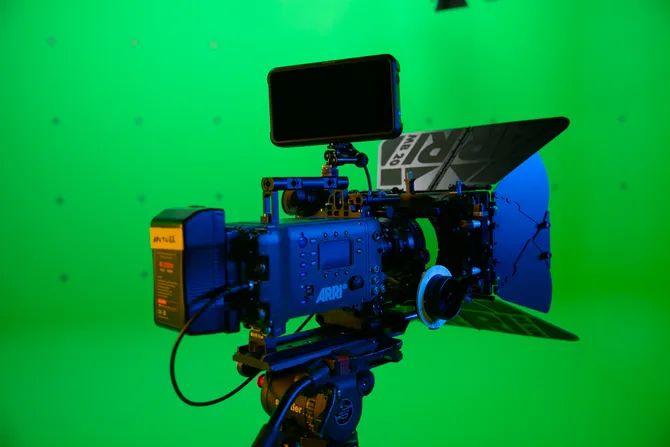 A film camera set up in front of a green screen.