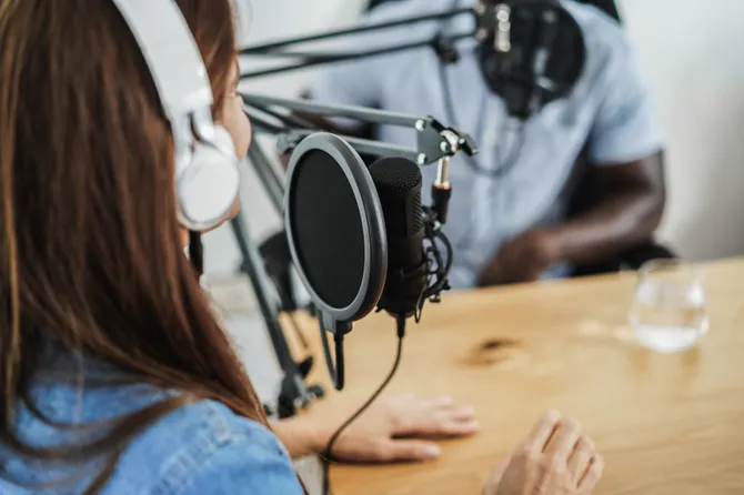 A man and a woman sat with headphones on speaking into a podcast microphone.