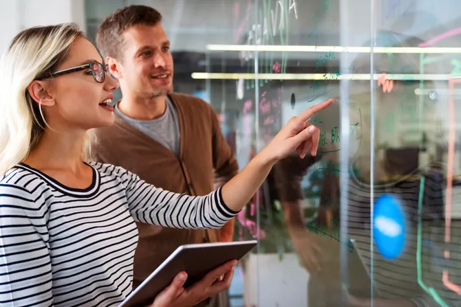 Two colleagues looking at notes on written on a glass screen