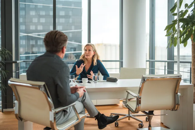 Two colleagues sat at a desk chatting