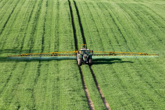 A tractor tending to crops with machinery in a large field.