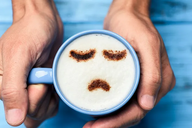 Blue cup of cappuccino with a sad face drawn with cocoa powder on the milk foam